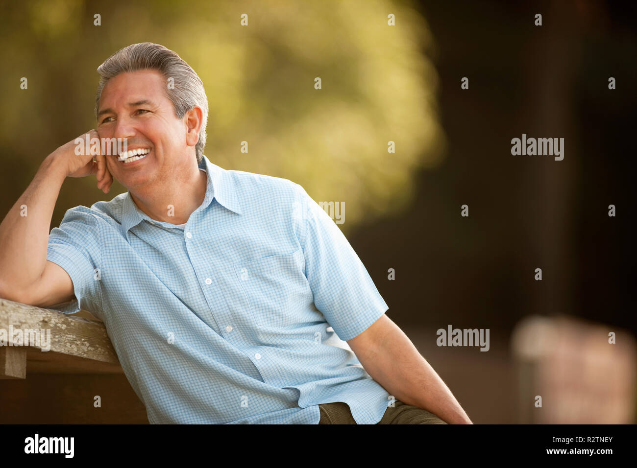 Reifer Mann lächelt, als er auf einem Picknicktisch lehnt. Stockfoto