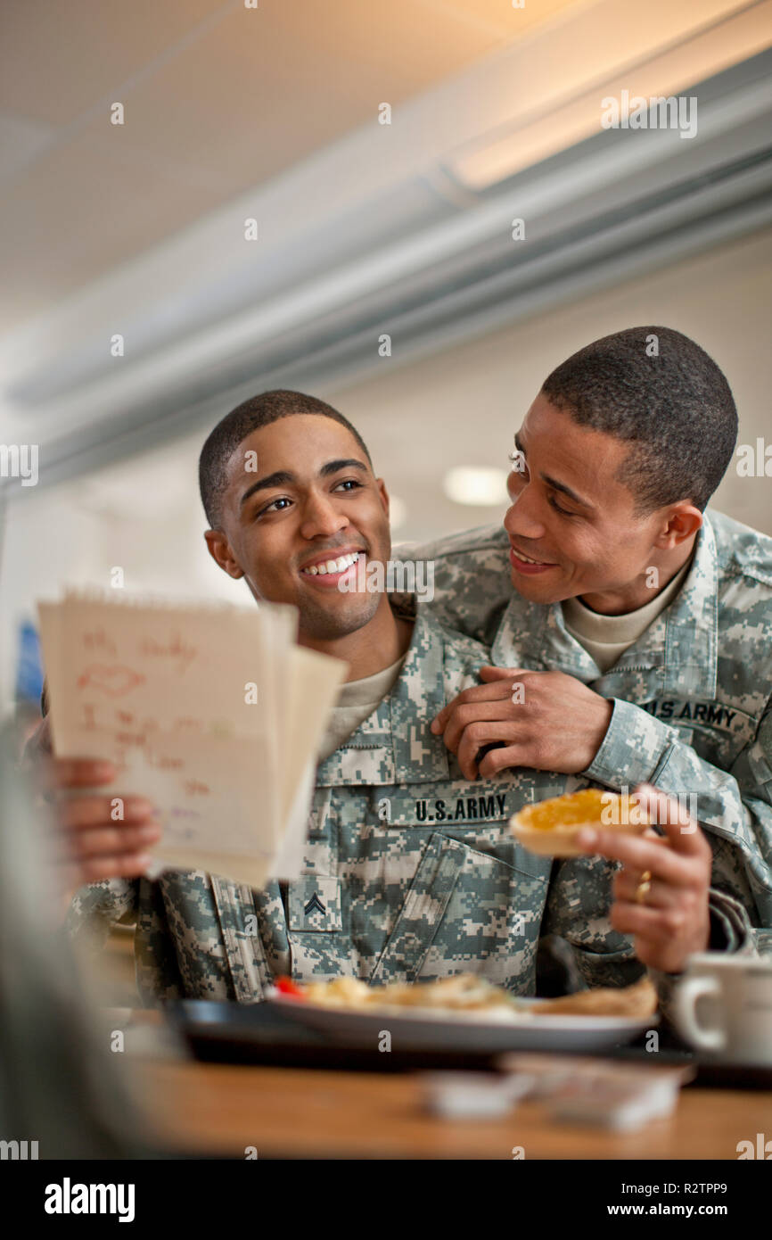 Junge Soldat schaut über die Schulter seines Freundes, als er einen Brief beim Frühstück liest. Stockfoto