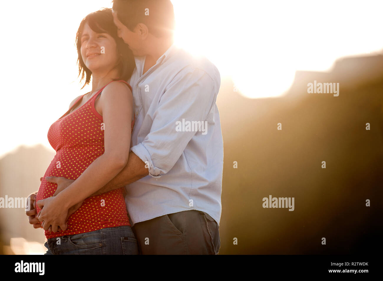 Twenty-Something Mann umarmt und küsst seine schwangere Frau. Stockfoto
