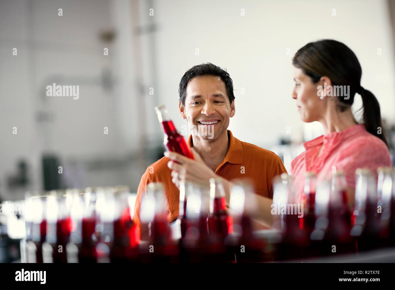 Zwei lächelnde Kollegen untersuchen eine Flasche aus einer Fertigungsstraße. Stockfoto