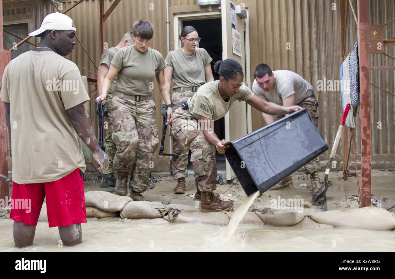 Ein Soldat verwendet einen Müll Wasser kann hinter einem sandsack Barriere vor einer Kaserne Gebäude zu retten Nach der schweren Unwetter im Camp Arifjan, Kuwait, 15. November 2018. Soldaten aus mehreren Einheiten zusammen auf die Überschwemmungen, die ihre Wohnräume beeinflusst hatten zu reagieren. Stockfoto