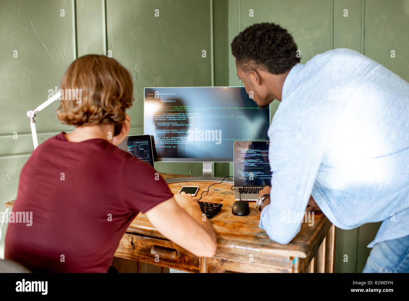 Zwei junge Programmierer mit Programmcode am Arbeitsplatz sitzen mit drei Monitoren im Büro auf die Grüne Wand Hintergrund Stockfoto