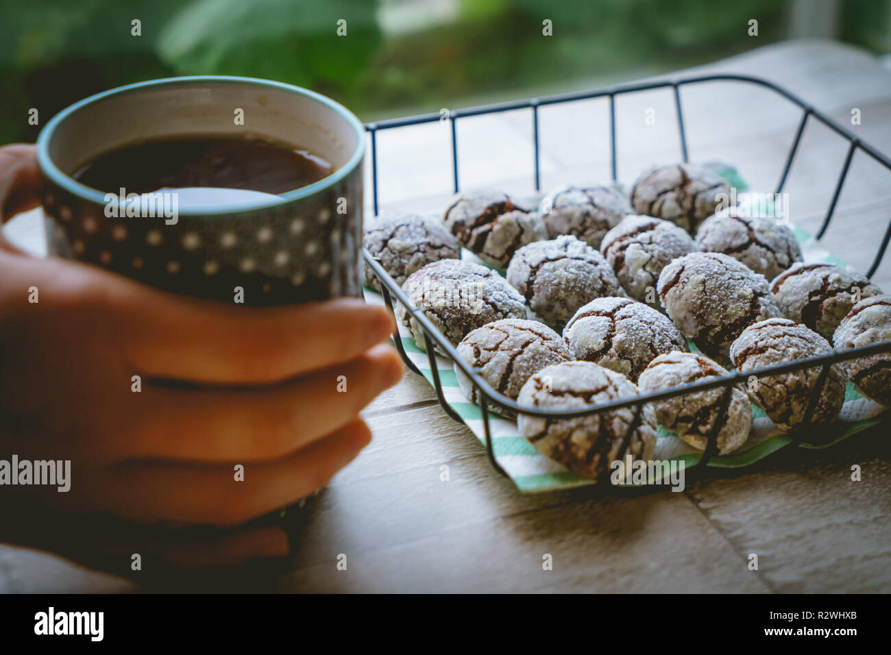 Schokolade crinkle Cookies in einem Korb mit einer Tasse Kaffee halten die Hände auf einen hölzernen Tisch. Nähe zu sehen. Querformat. Stockfoto