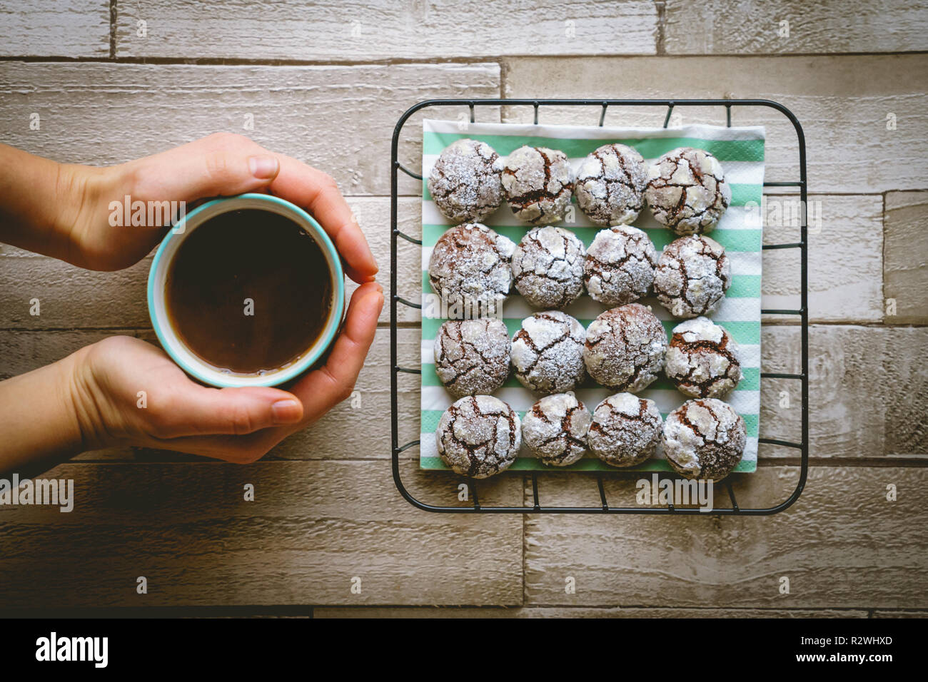 Schokolade crinkle Cookies in einem Korb mit einer Tasse Kaffee halten die Hände auf einen hölzernen Tisch. Ansicht von oben. Querformat. Stockfoto