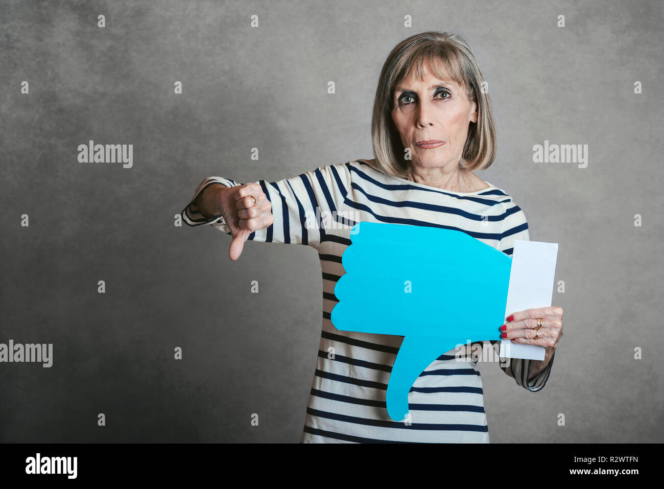 Senior woman holding eine Abneigung Symbol auf grauem Hintergrund Stockfoto