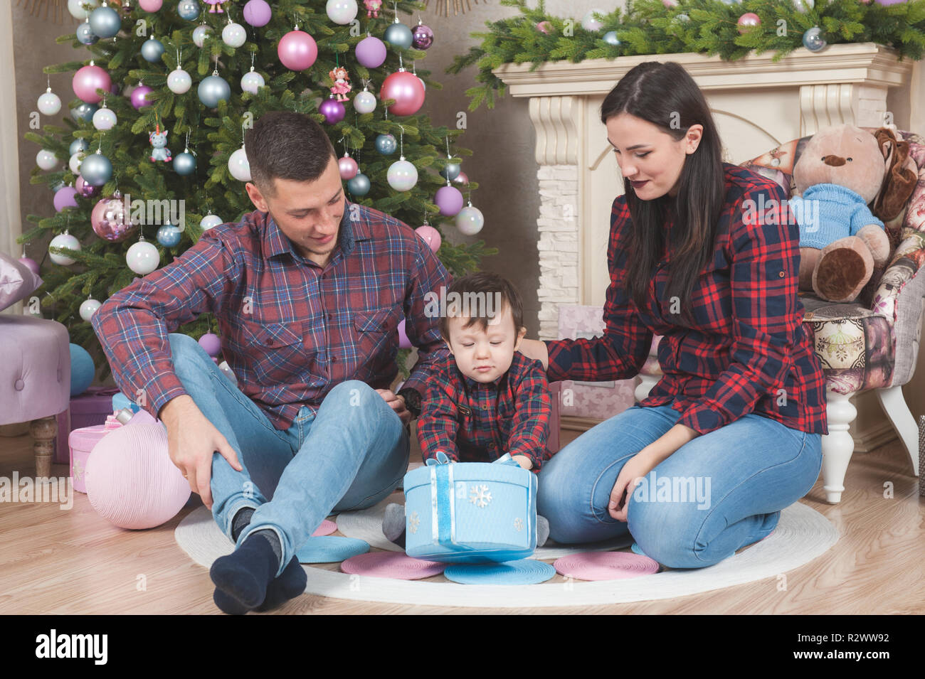 Glückliche Mutter und Vater sitzen und das kleine Kind mit Box von Geschenk Weihnachten Stockfoto