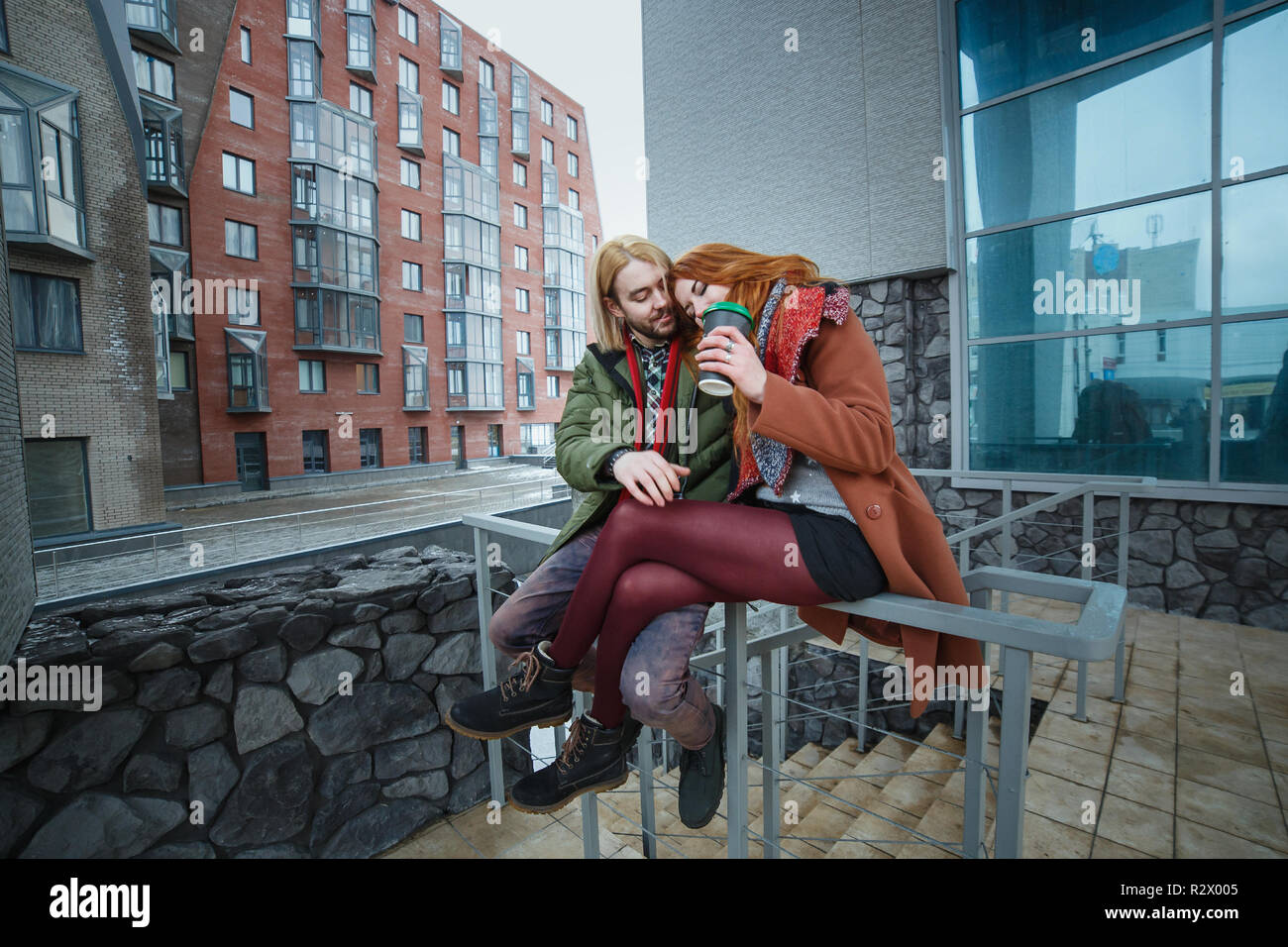 Junge europäische Paar Spaß im Winter im städtischen Hintergrund. Punks oder Hipster Style. Rothaarige Mädchen in roten Schal bekleidet ist, braunes Fell, kurze Shorts ein Stockfoto