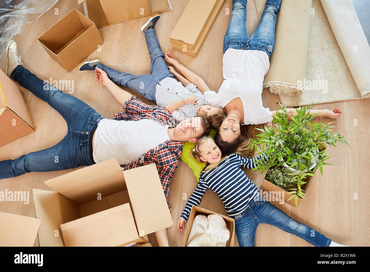Familienangehörige, die in ihre neue Heimat die Heimat glücklich liegt zwischen Umzugskisten auf dem Boden Stockfoto