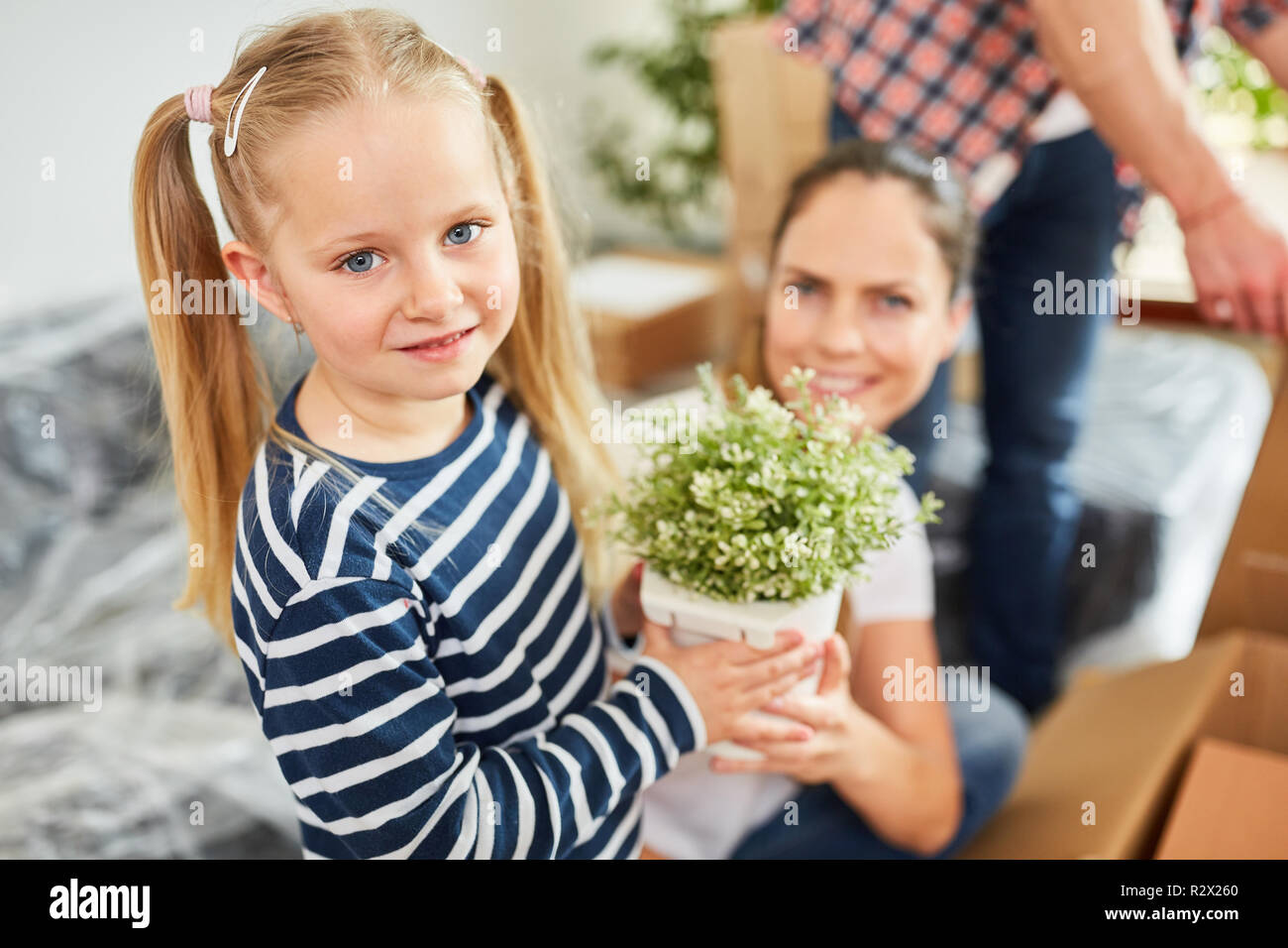 Kleines Mädchen hilft Eltern zu bewegen, während die Pflanzen Stockfoto