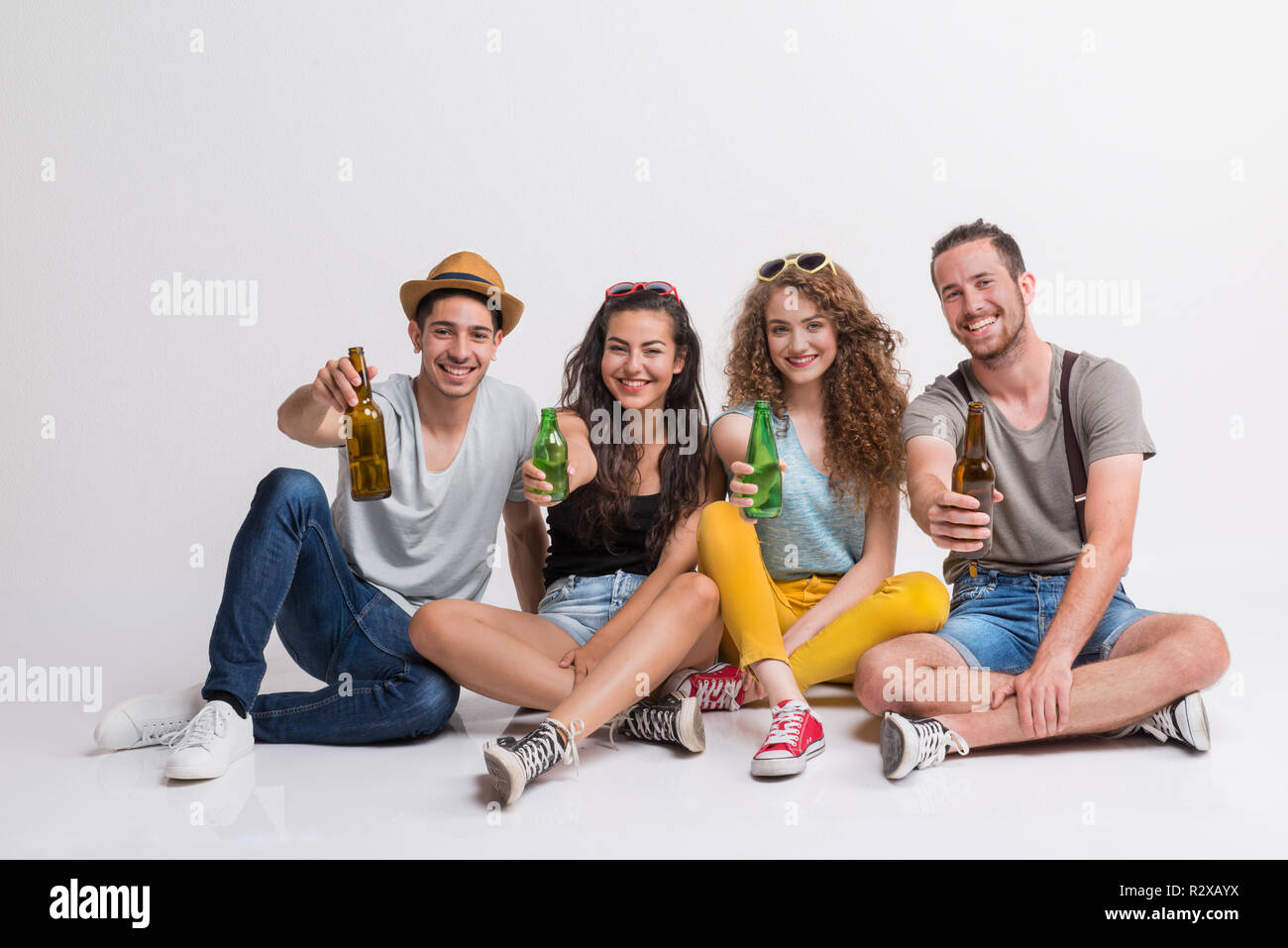 Portrait von freudige junge Gruppe von Freunden mit Flaschen auf dem Boden sitzend in einem Studio. Stockfoto