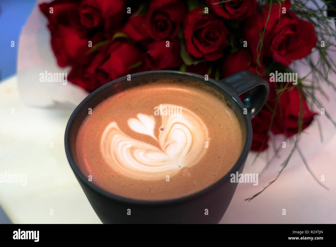 In Herzform Creme auf Kaffee mit roten Rosen Blumenstrauß auf dem Tisch Stockfoto