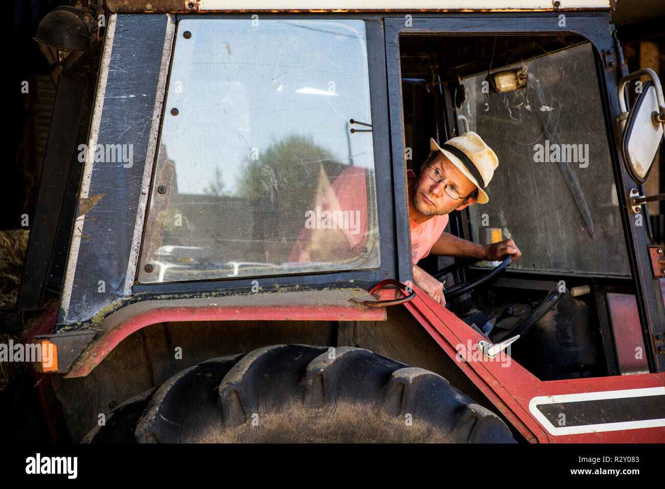 Betriebsinhaber, die Stroh Hut und Brille fahren roten Traktor. Stockfoto
