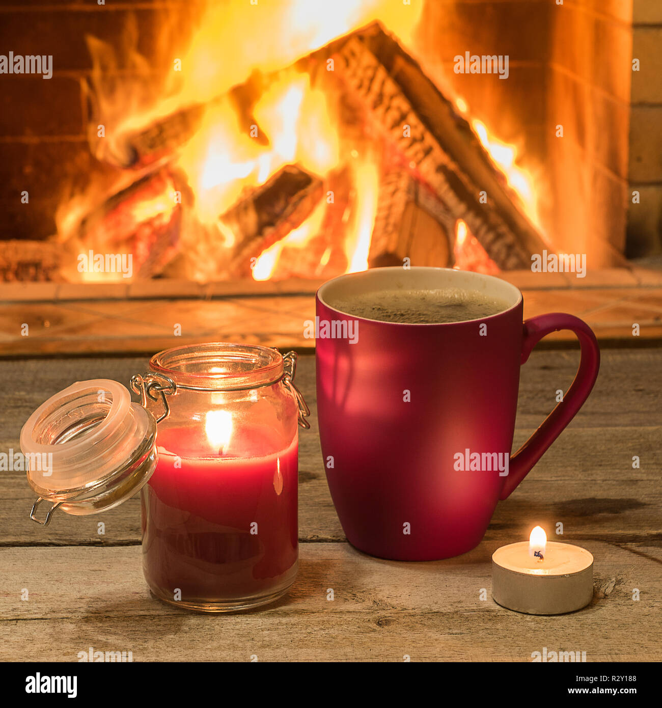 Becher mit heißem Tee und Kerzenschein in der Nähe von gemütlichem Kamin, im Landhaus, winter Urlaub, horizontal. Stockfoto