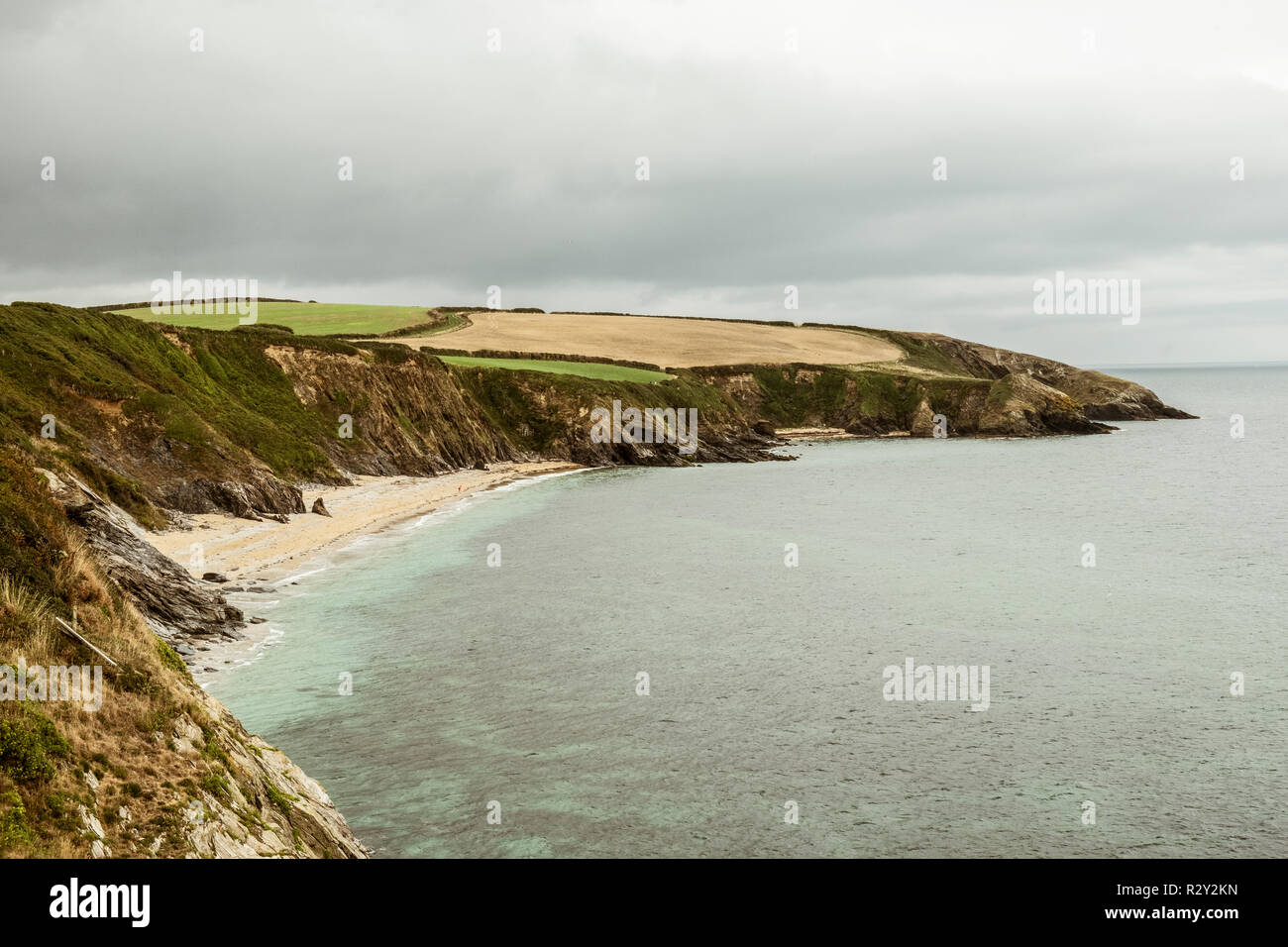 Blick entlang der Küste mit Felsen und Sandstrand und einem Vorgewende bedeckt grauer Himmel. Stockfoto