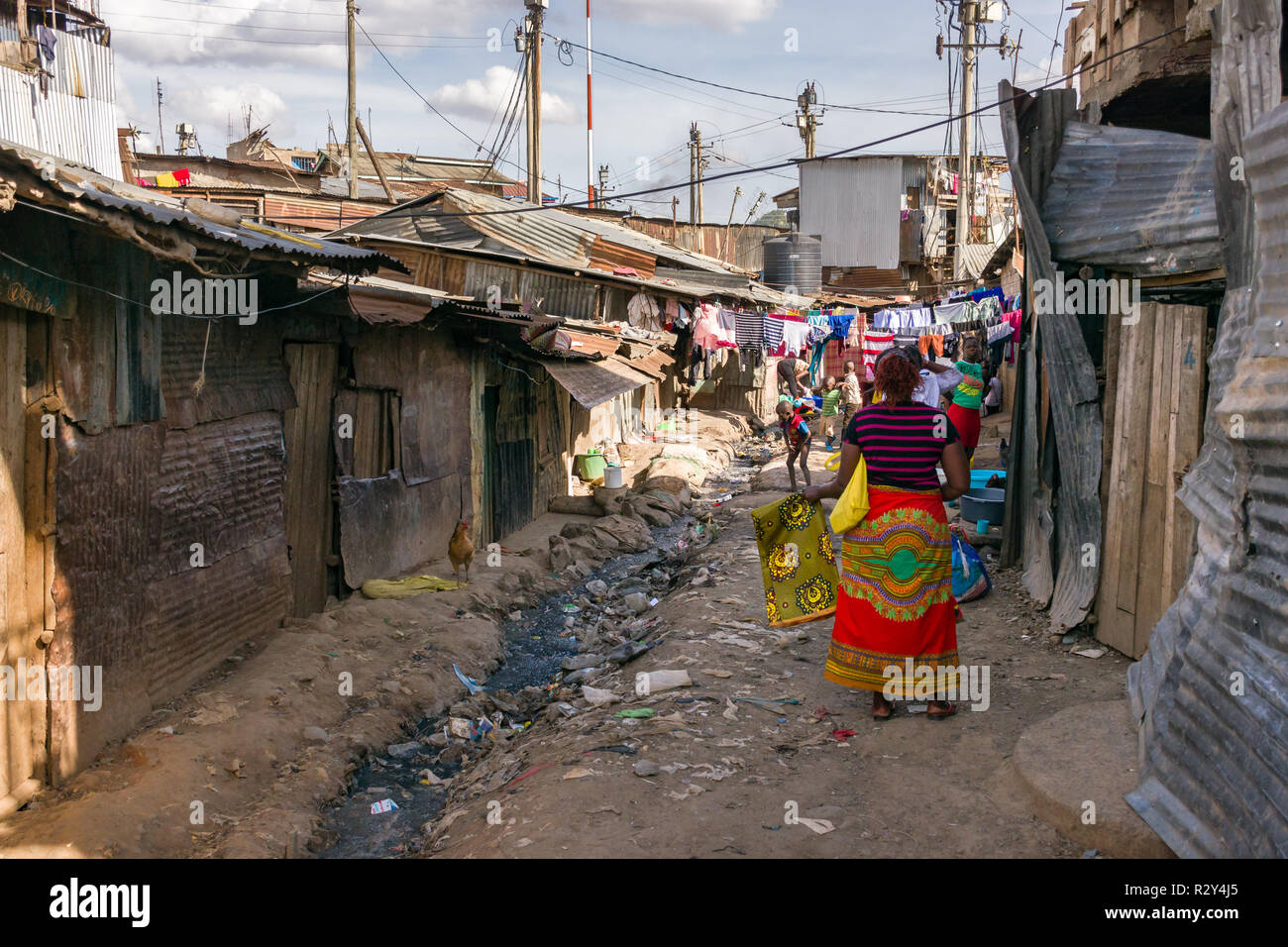 Die kenianischen Frauen, die Kleider waschen und spielende Kinder in einer Seitengasse mit Wellblech Hütten und offenen Abwasser stream gesäumt, die Mathare Slum, Kenia Stockfoto