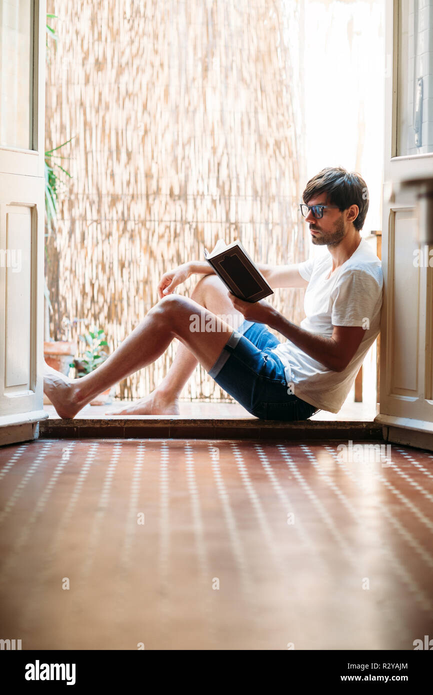 Junger Mann lesen Buch auf dem Balkon zu Hause sitzen. Entspannen Sie sich und Wochenende Konzept Stockfoto