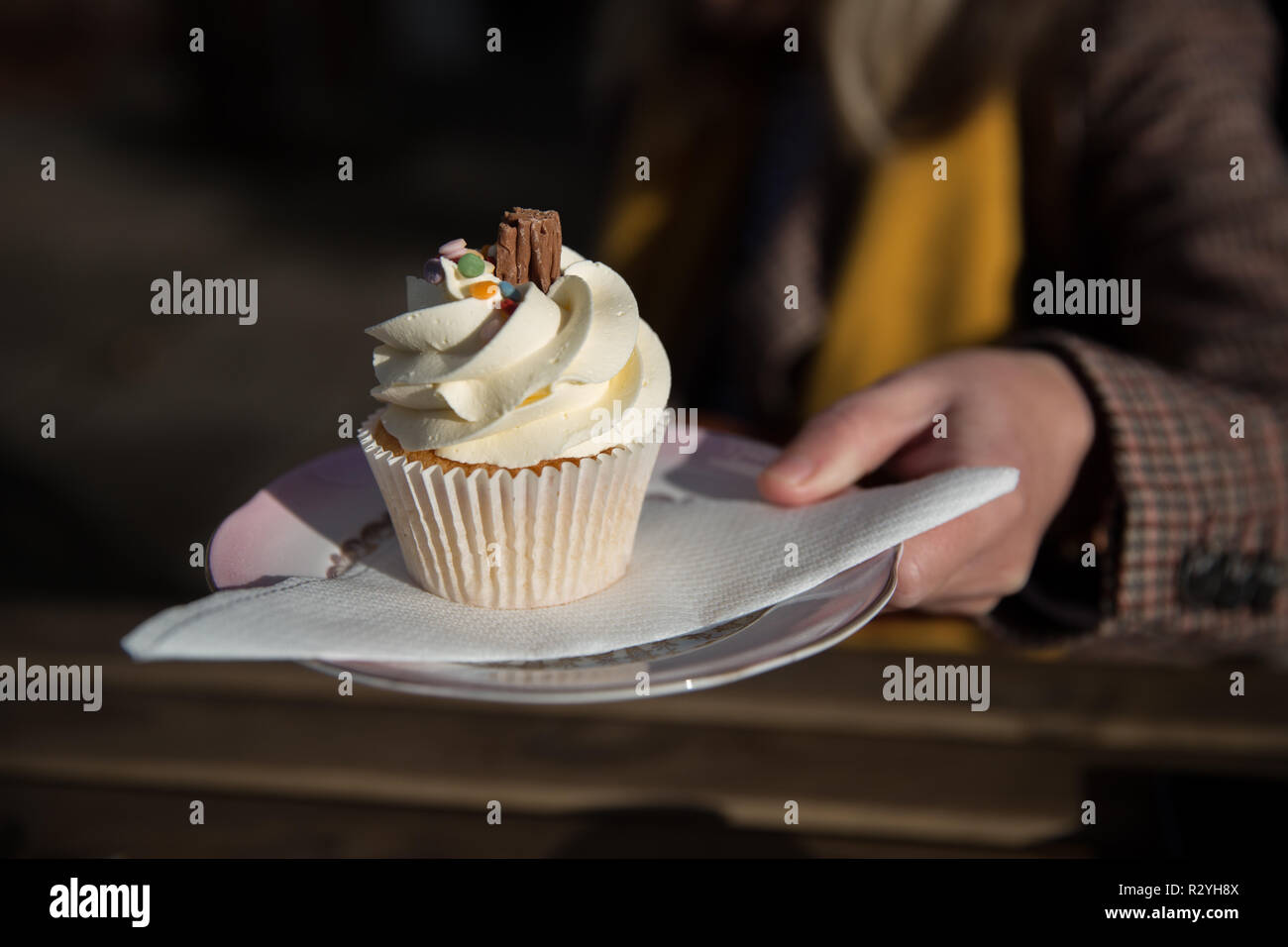 Eine Nahaufnahme von einem Mädchen hand Halten eines leckeren Vanilla Cupcake oder Muffin mit Wirbelte Zuckerguß auf einen Teller und Servietten mit Kopie Raum Stockfoto