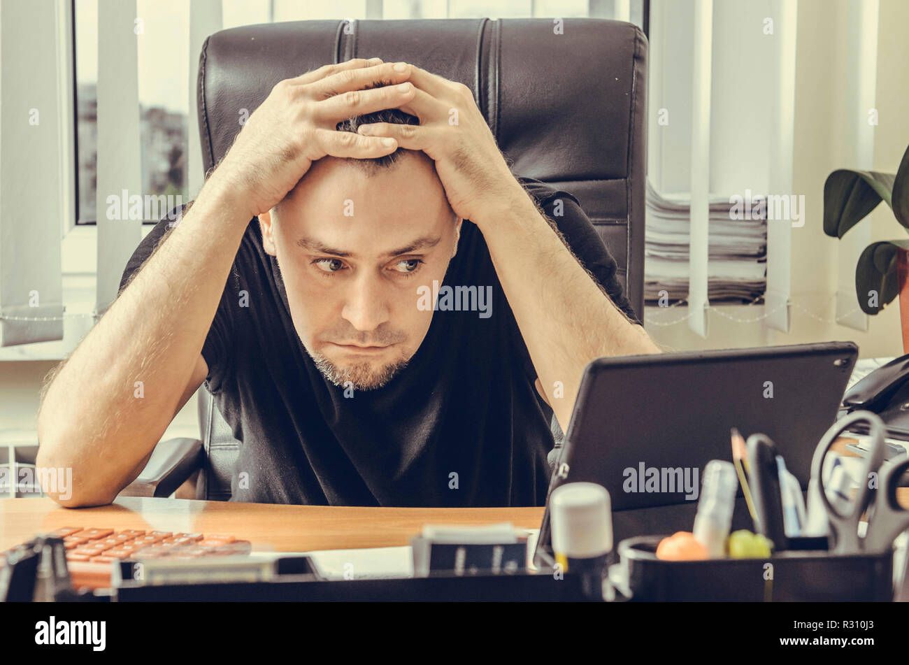 Schockiert Geschäftsmann in einem Stuhl sitzend an seinem Schreibtisch und Blick auf einem Tablet Bildschirm Stockfoto