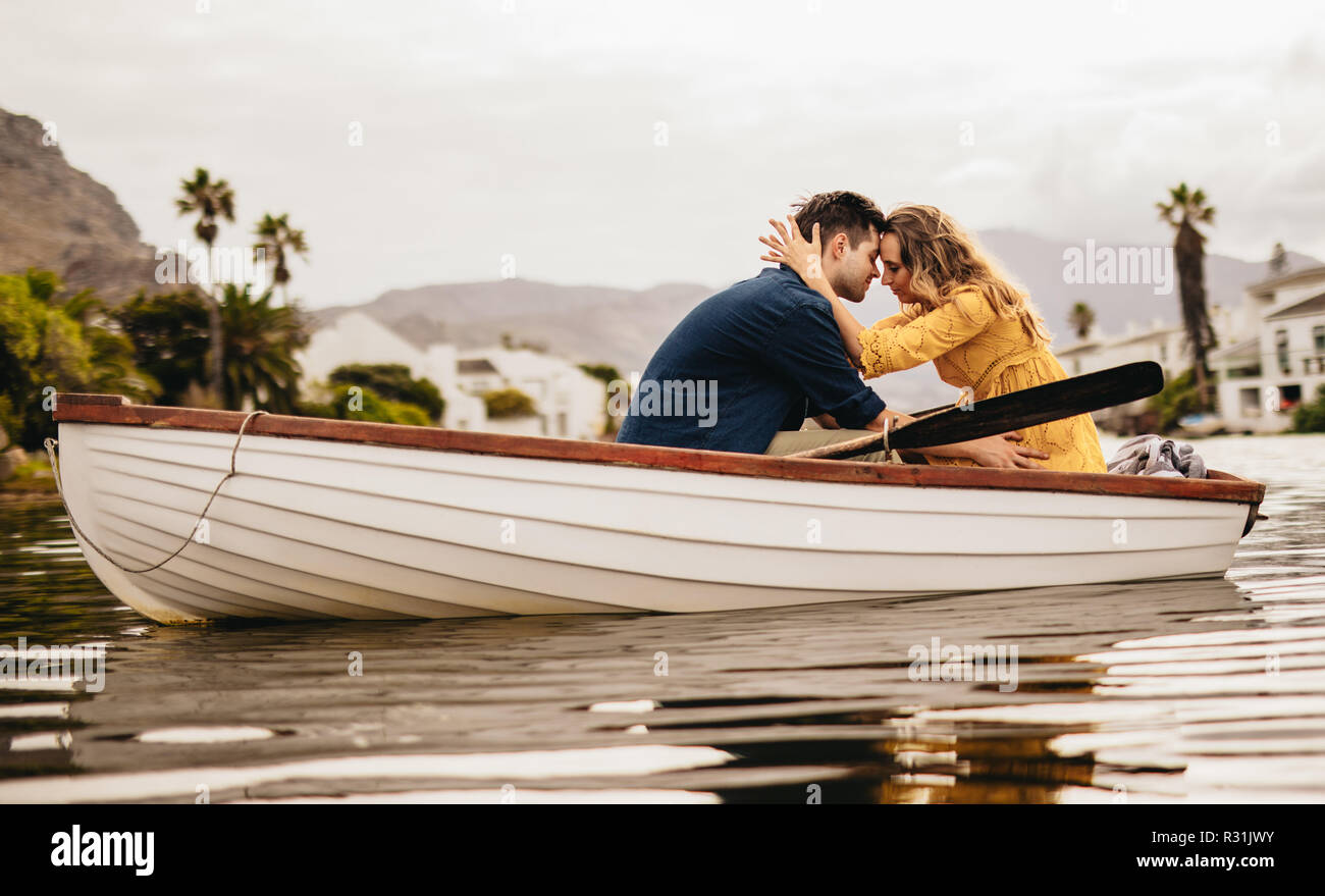 Junges Paar sitzen gemeinsam in einem Boot ihre Köpfe zu berühren. Paar in Liebe auf einem Boot Datum in einem See mit Hügeln und Häuser im Hintergrund. Stockfoto