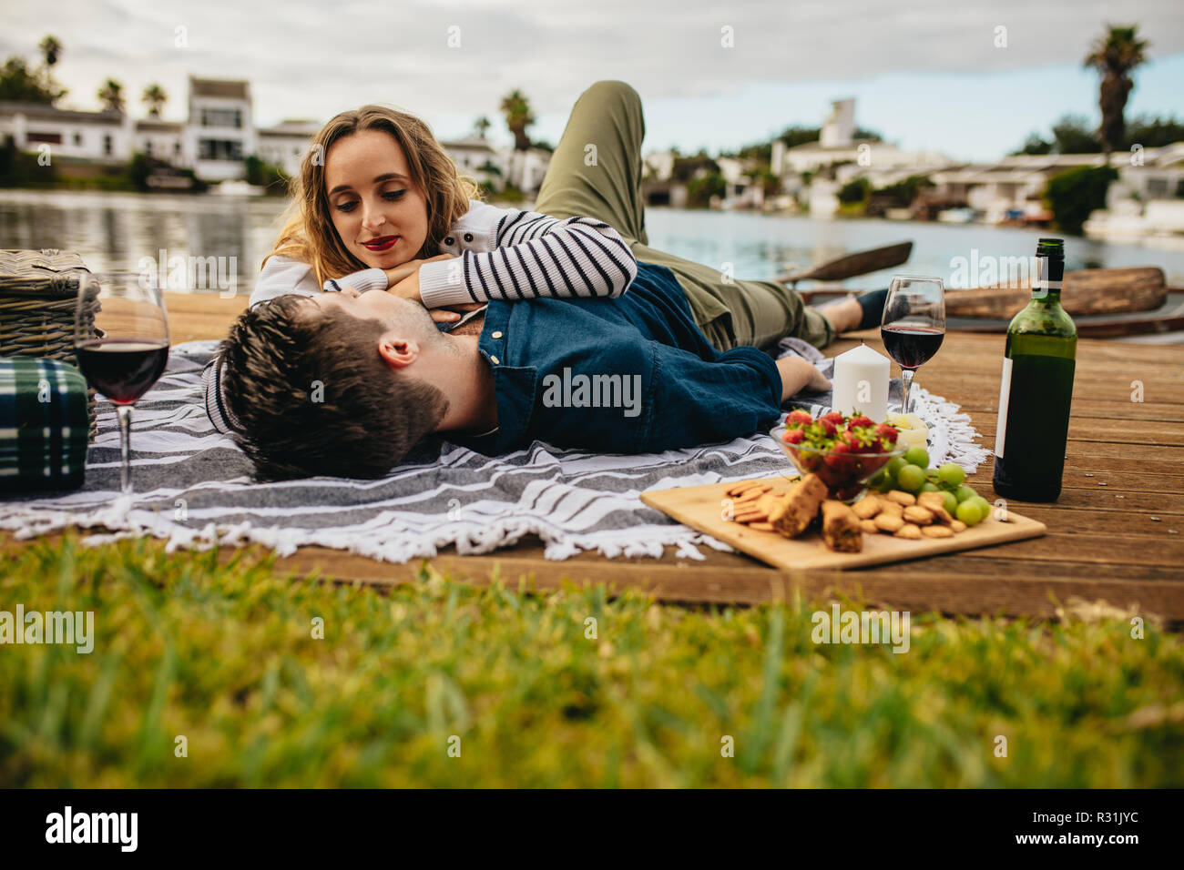 Mann liegen auf dem Dock in der Nähe der See mit seiner Freundin ruht ihre Hände auf seine Brust. Romantisches Paar auf ein Datum in der Nähe von einem See genießen Sie Speisen und Getränke Stockfoto