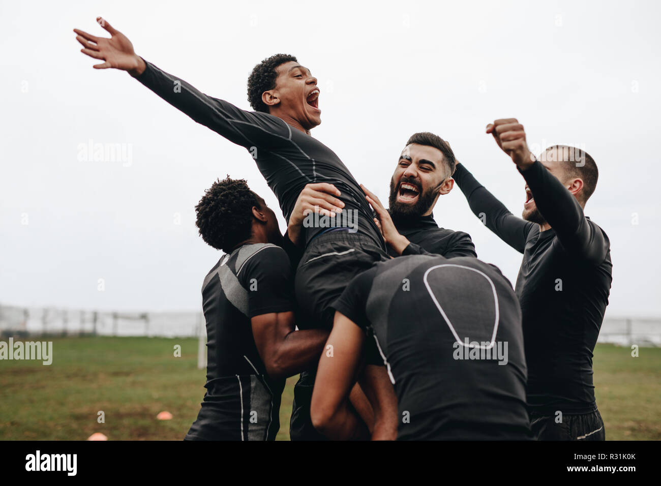 Gruppe von Fußball-Spieler feiern gemeinsam ein Ziel stehend auf dem Feld. Mannschaftskameraden feiern ein Ziel durch Anheben einer Player und jauchzen in der Freude. Stockfoto