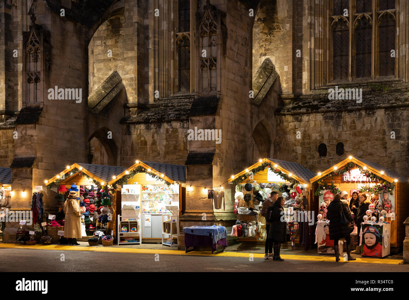 Gotische Kathedrale von Winchester bei Nacht und Weihnachtsmarkt in der mittelalterlichen Stadt Winchester mit Weihnachtseinkäufern, die durch hölzerne Chalets bummeln. England Stockfoto