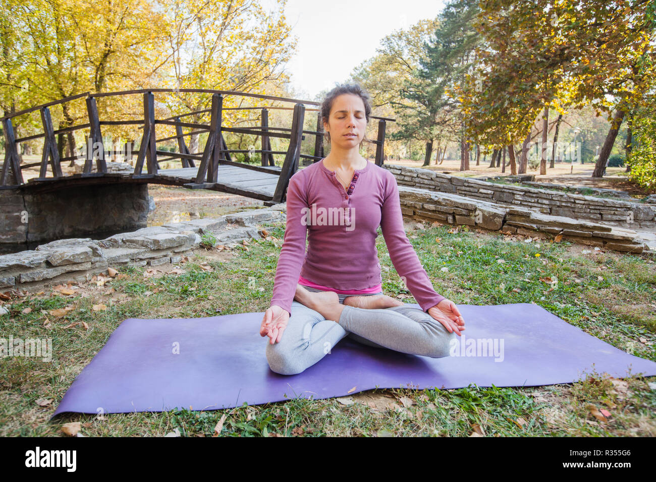 Gesunde, junge schöne Frau Praktizieren von Yoga und Meditation im Lotussitz Padmasana, Übung, Sitzen auf den Fitness Matte im Park im Herbst Tag. Stockfoto