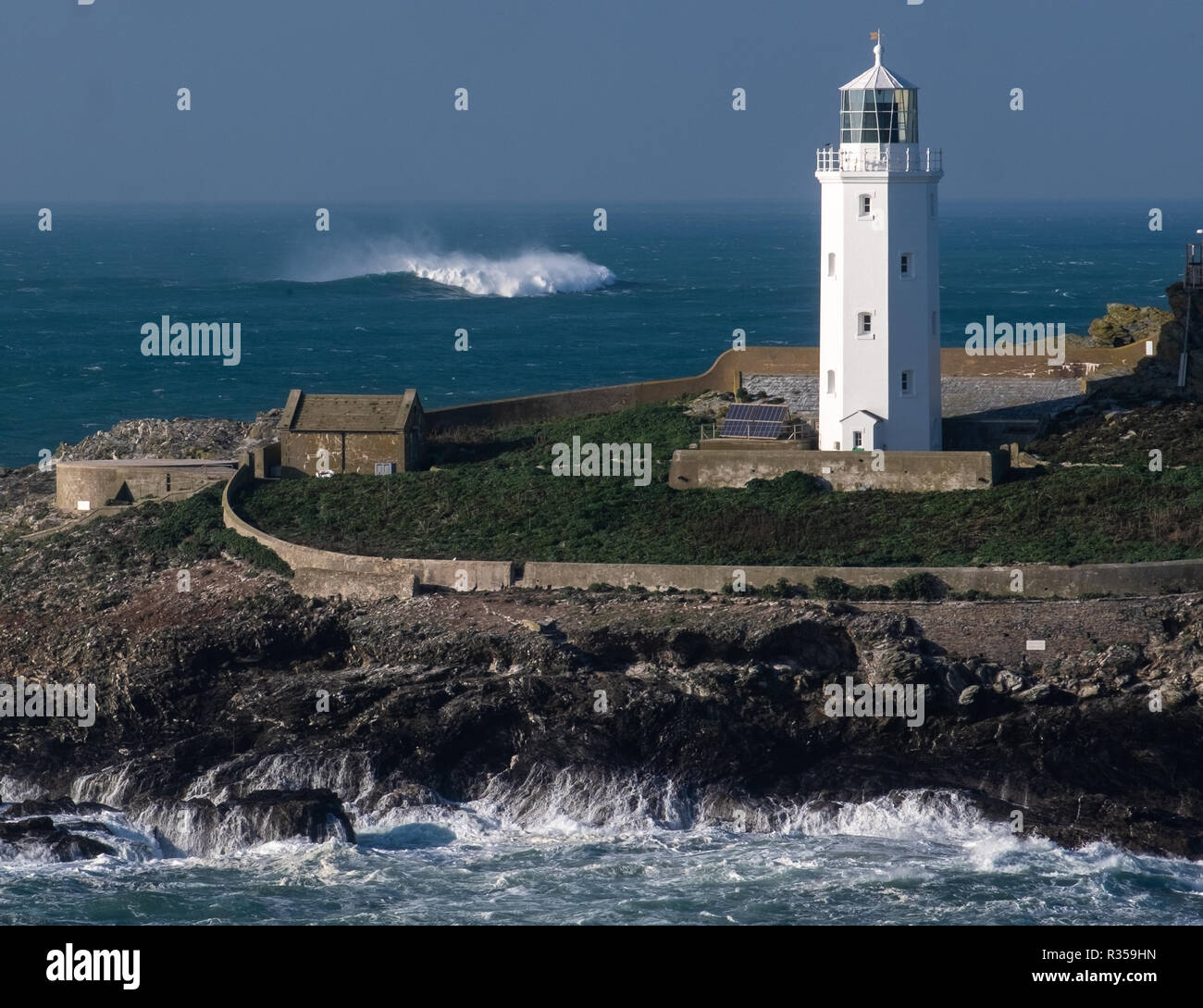 Nahaufnahme von Godrevy Leuchtturm, Teil der Insel und der kleine alte Wohnungen an der Seite. Brechende Welle im Meer hinter sich. Stockfoto