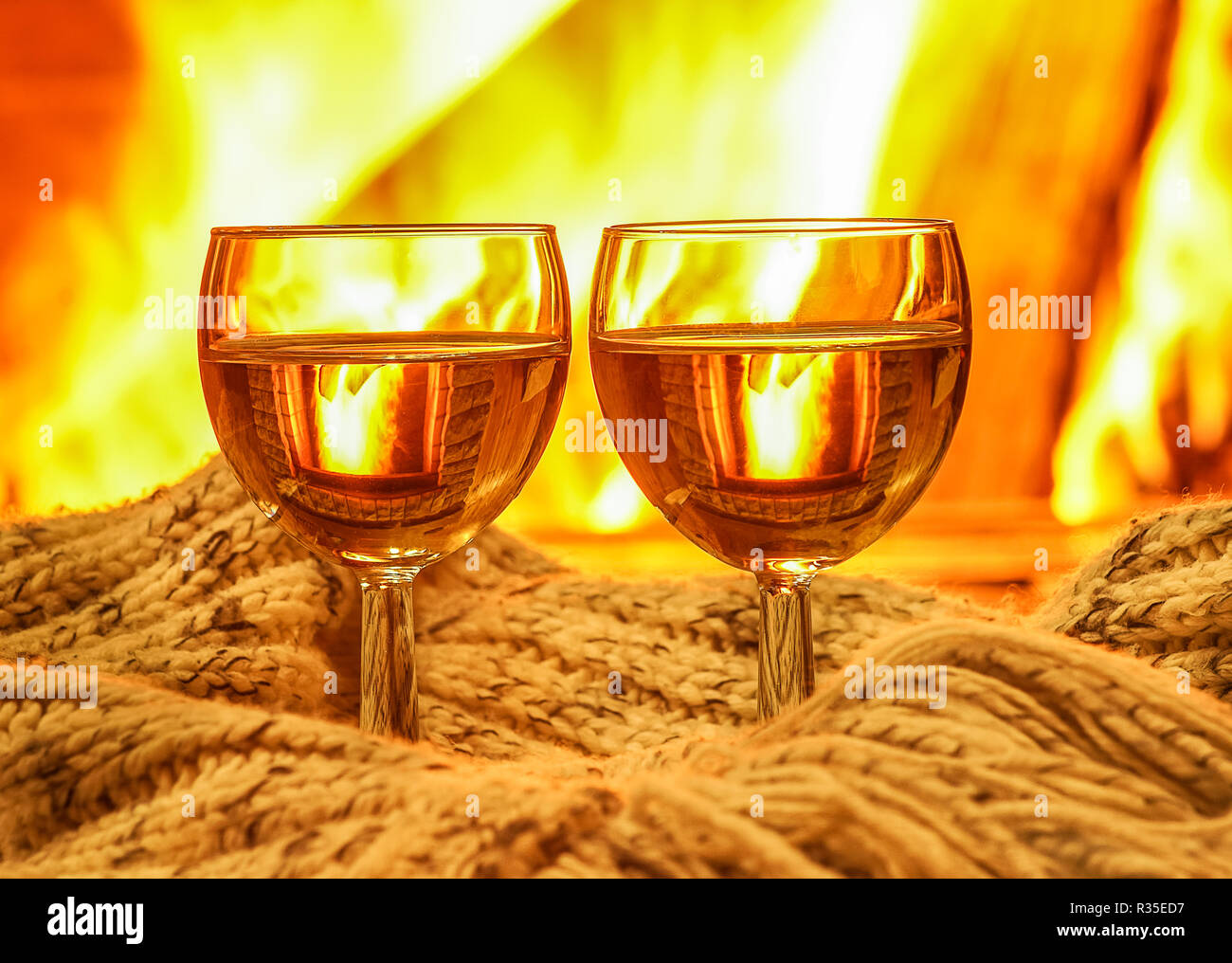 Zwei Gläser Weißwein und wolle etwas gegen gemütlichen Kamin Hintergrund, Winterurlaub im Landhaus, horizontal. Stockfoto