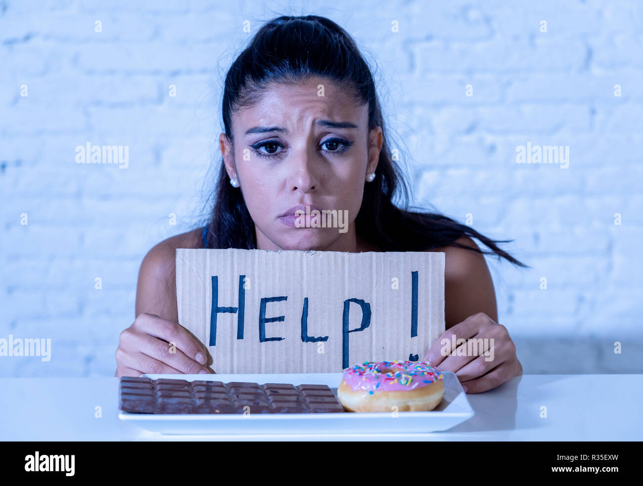 Junge besorgt Latin Frau Gefühl versucht und schuldig, Schokolade und Donuts um Hilfe zu bitten, in der Diät Kalorien Zucker Ernährung Essen ein Stockfoto