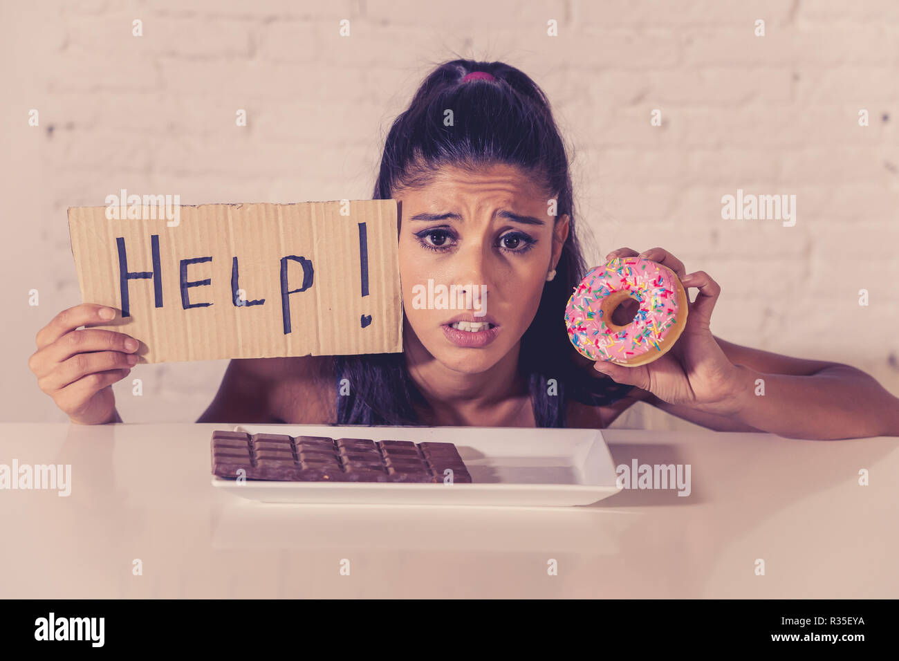Junge besorgt Latin Frau Gefühl versucht und schuldig, Schokolade und Donuts um Hilfe zu bitten, in der Diät Kalorien Zucker Ernährung Essen ein Stockfoto