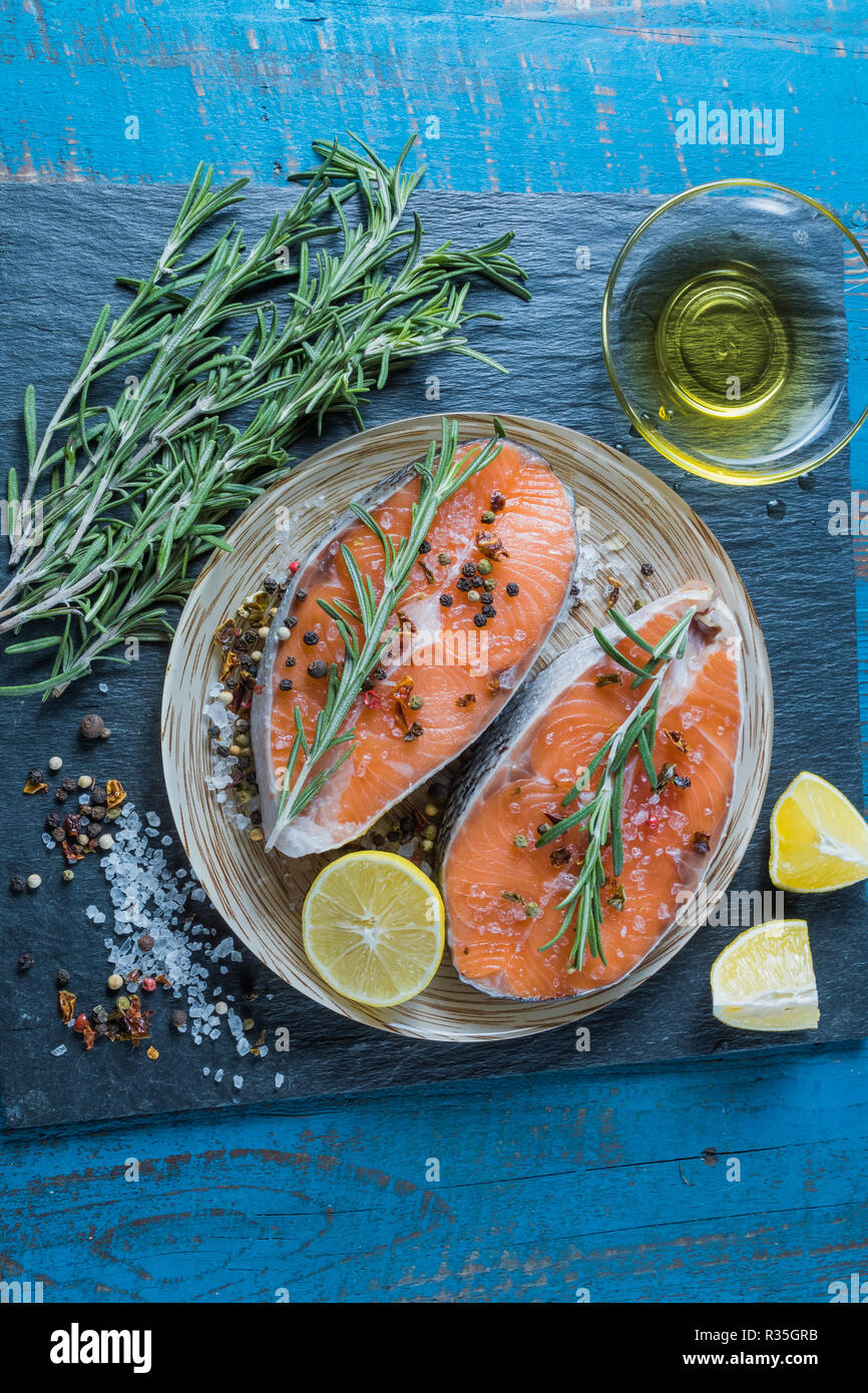 Rohe frische Lachs Fisch vor dem Kochen, mit Zitronensaft und Gewürzen, auf Platte, über alte blaue Holz- Hintergrund. Stockfoto