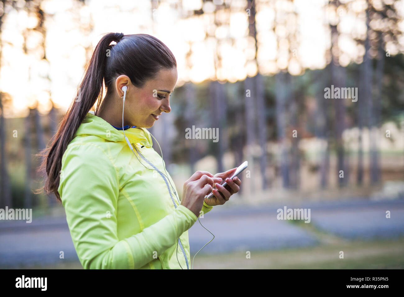 Eine junge Läuferin im Freien im Herbst Natur, mit Smartphone. Stockfoto
