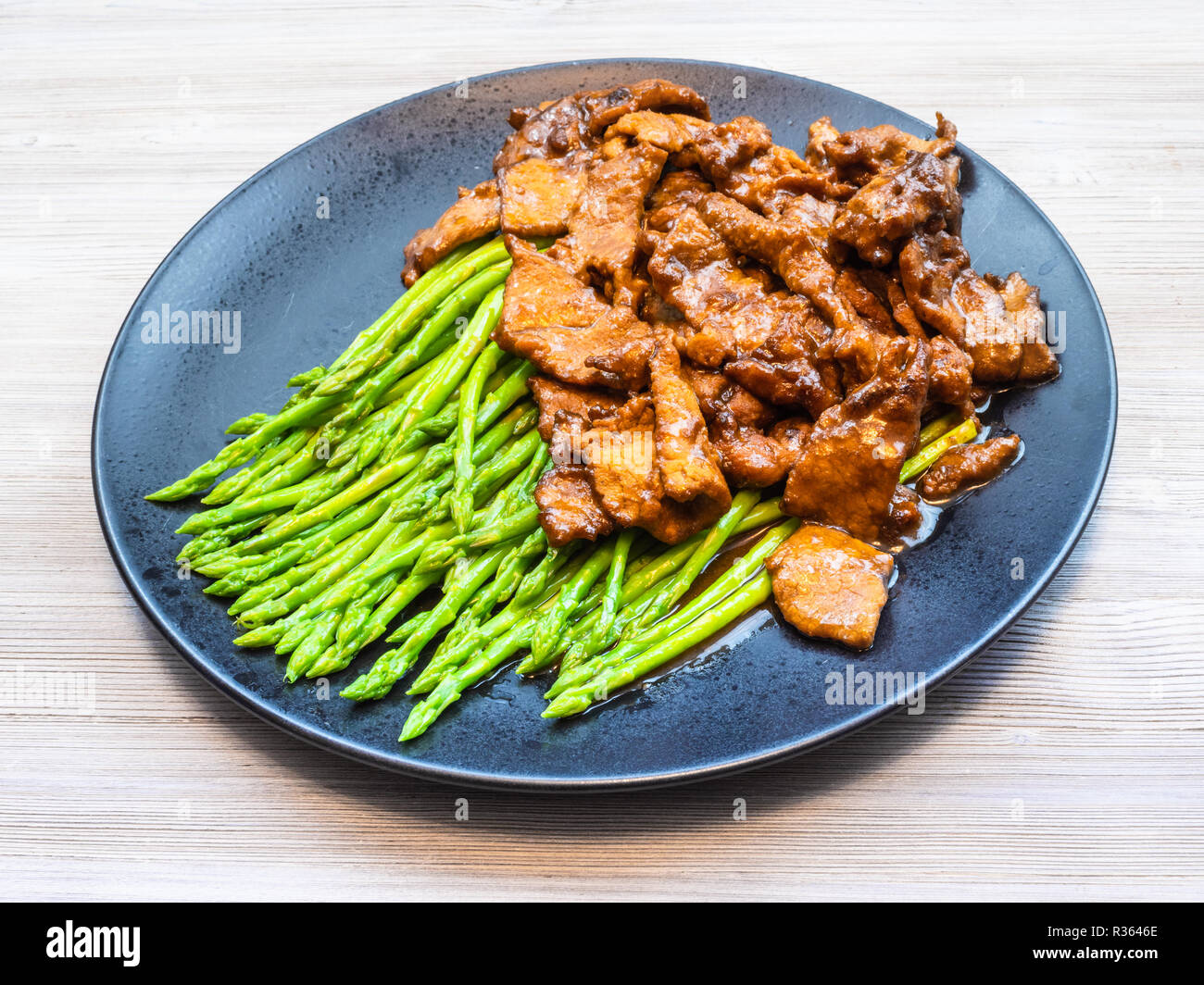 Chinesische Küche Teller - Rindfleisch gebraten in Sojasauce mit gekochten Spargel auf Schwarz auf Grau Tabelle Stockfoto