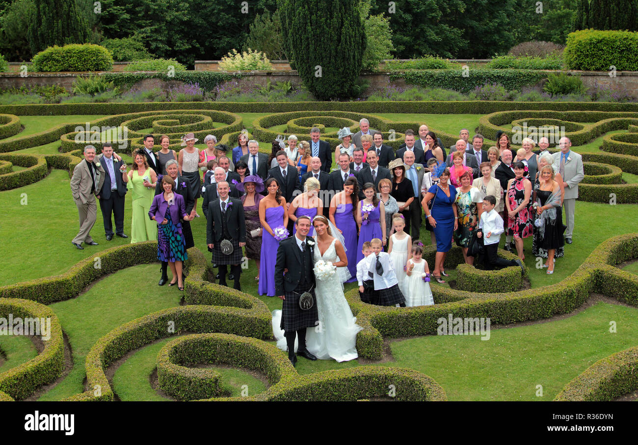 Die Braut und der Bräutigam und alle Gäste bei ihrer Hochzeit, für ein Foto im Garten neben der Schauplatz nach der Zeremonie in Schottland dar. Stockfoto