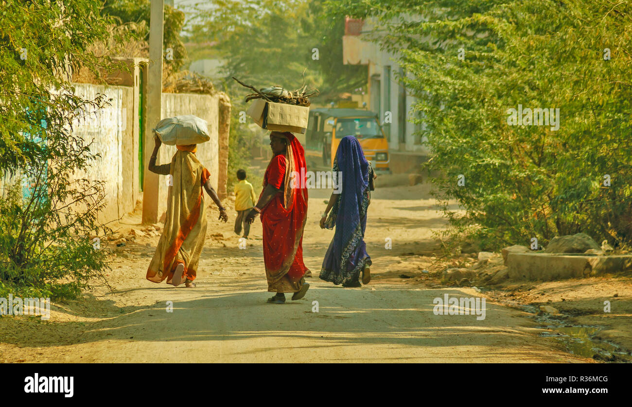 RAJASTHAN INDIEN staubige Straße und drei Frauen mit bunten Saris und SCHWEREN LASTEN AUF DEM KOPF Stockfoto