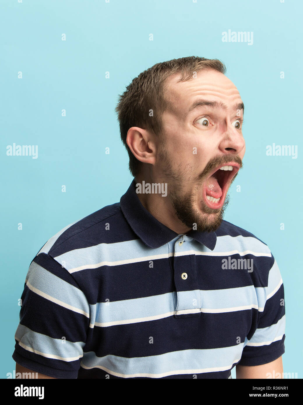 Das überrascht und erstaunt junge Mann schreiend mit offenen Mund auf blauem Hintergrund isoliert. Konzept der Schock Gesicht emotion Stockfoto