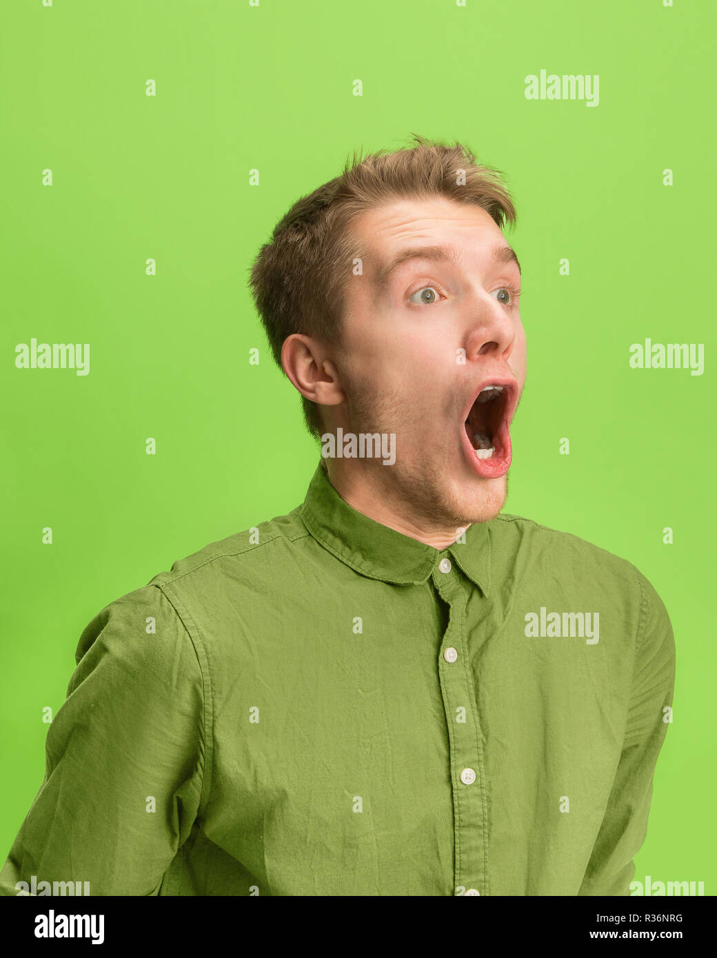 Das überrascht und erstaunt junge Mann schreiend mit offenen Mund auf grünem Hintergrund isoliert. Konzept der Schock Gesicht emotion Stockfoto