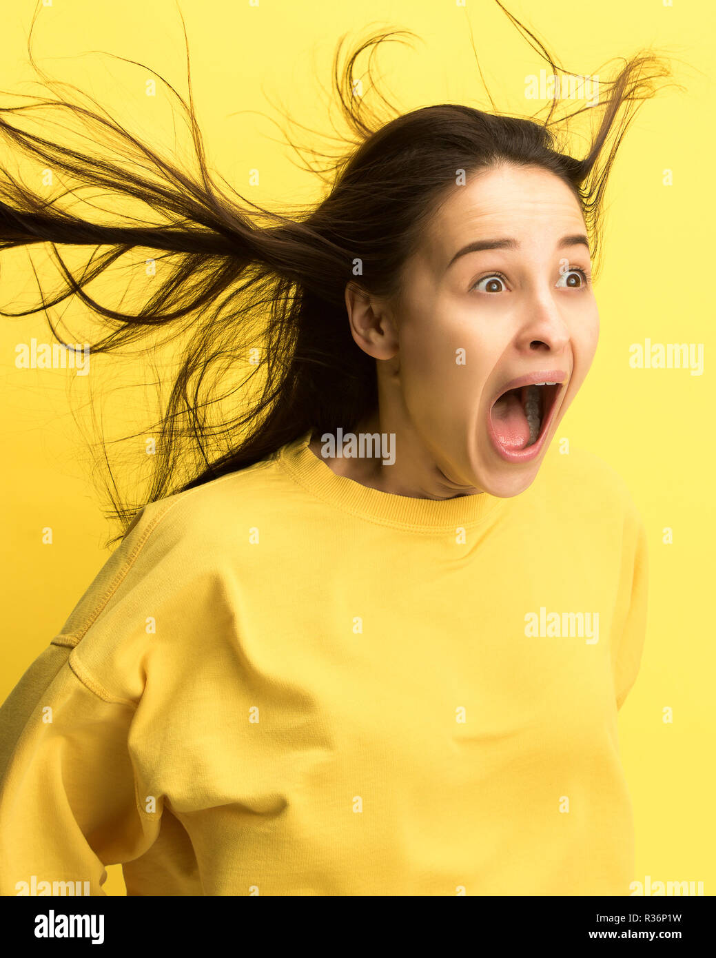 Das überrascht und erstaunt junge Frau schreiend mit offenen Mund auf gelben Hintergrund isoliert. Konzept der Schock angesichts der menschlichen Emotion Stockfoto