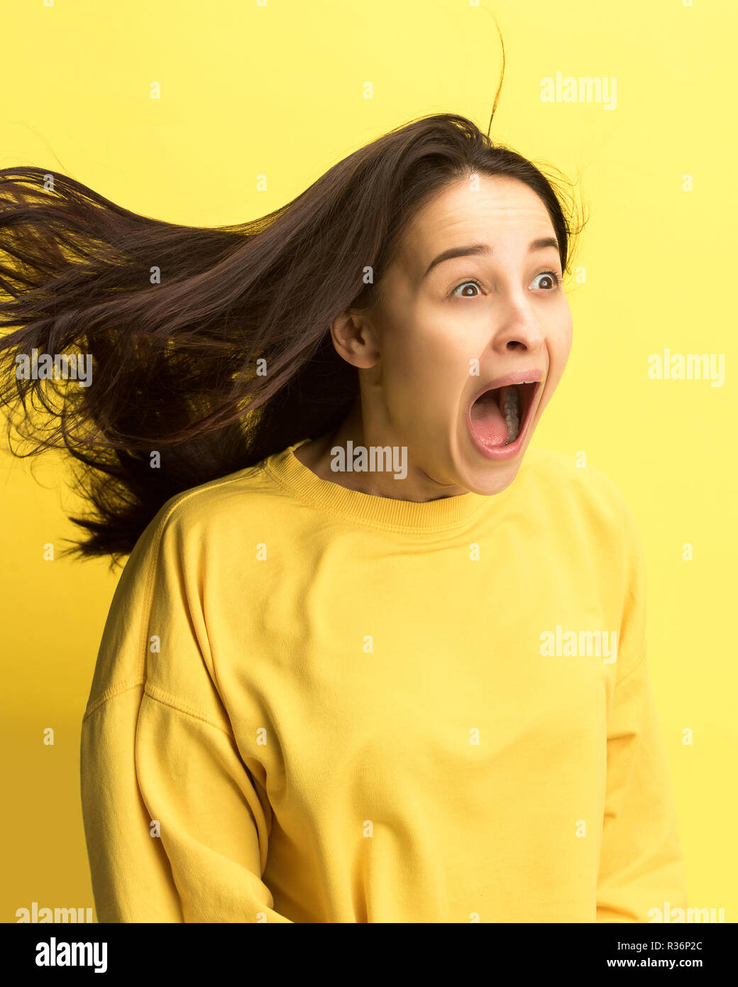 Das überrascht und erstaunt junge Frau schreiend mit offenen Mund auf gelben Hintergrund isoliert. Konzept der Schock angesichts der menschlichen Emotion Stockfoto