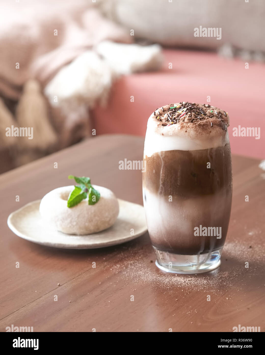 Ein Glas Milch Schokolade Frappe mit Schlagsahne auf Holztisch mit Blur Weißzucker Donut auf dem Tisch Stockfoto