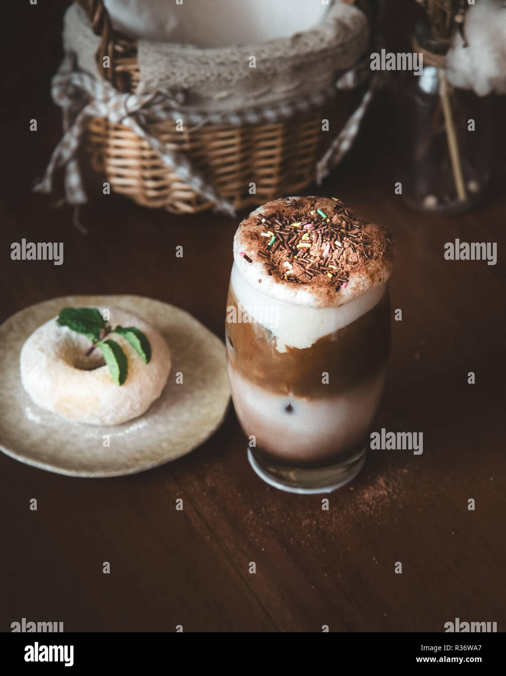 Schokolade Milchshake mit Kaffee und bunten Streuseln Zucker als Topping und Unschärfe Donut und Minzeblatt auf hölzernen Tisch im Cafe Stockfoto