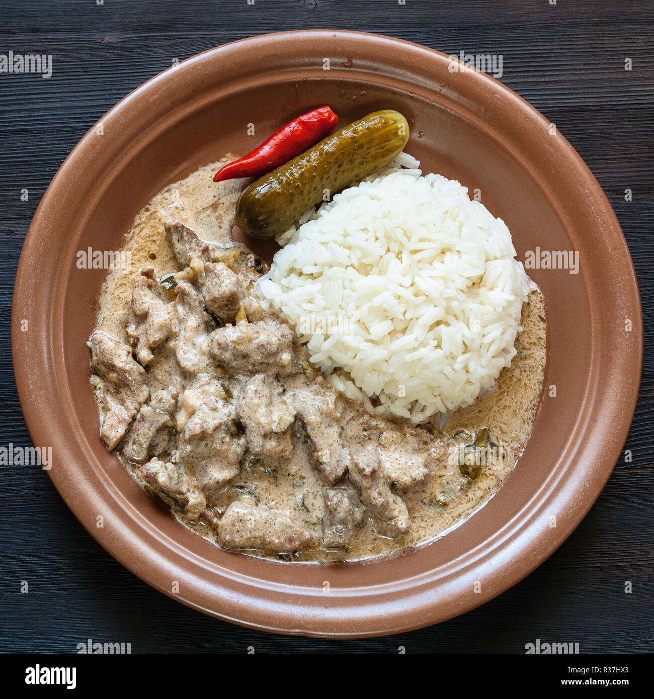 Russische Küche Geschirrspüler braun Platte mit Beef Stroganoff (Beef Stroganov, Befstroganov) Stück Fleischeintopf in Sauerrahm und gekochtem Reis aus dunklem Holz Stockfoto