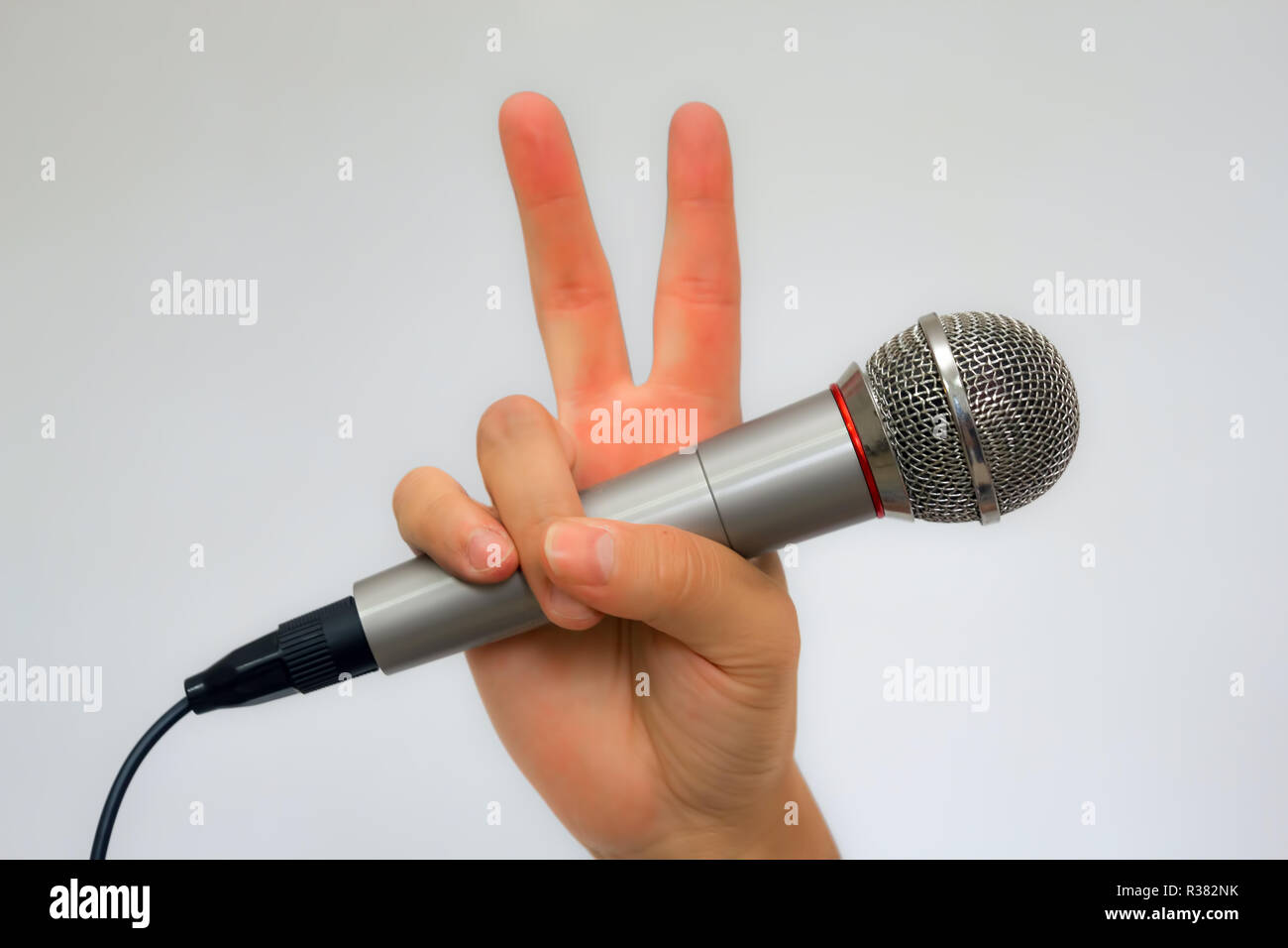 Eine Hand mit einem Mikrofon und zwei Finger Sieg Stockfoto