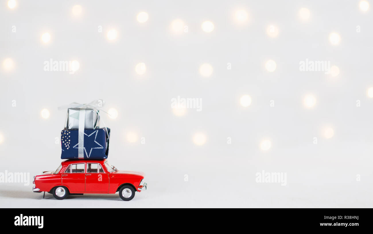 Rote Spielzeugauto mit einem Weihnachtsgeschenke auf dem Dach, Girlande bokeh auf dem Hintergrund, geringe Tiefenschärfe. Stockfoto