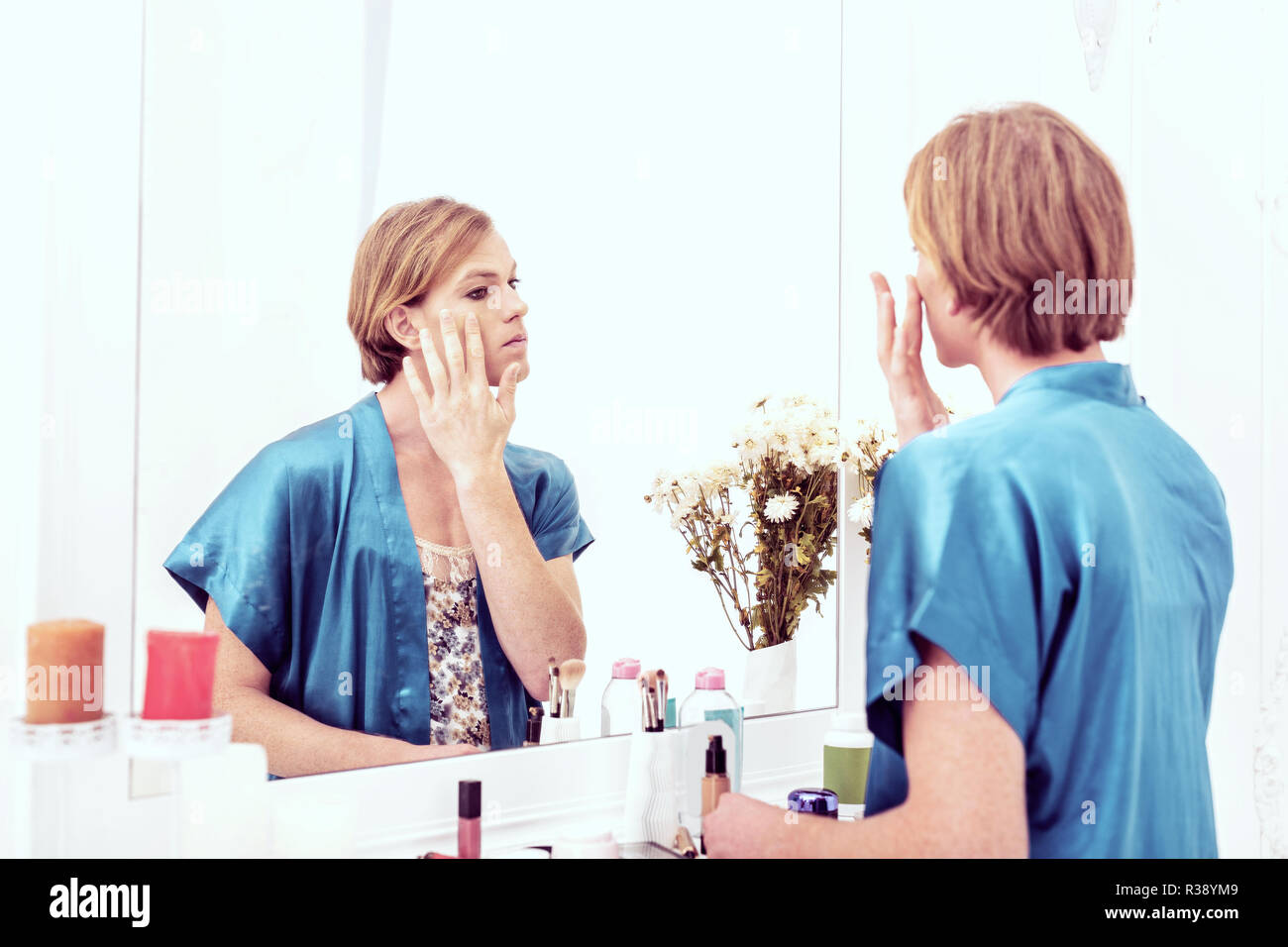 Ansprechende crossdresser in blauer Seide weiblich Robe bleiben gegen den Spiegel Stockfoto