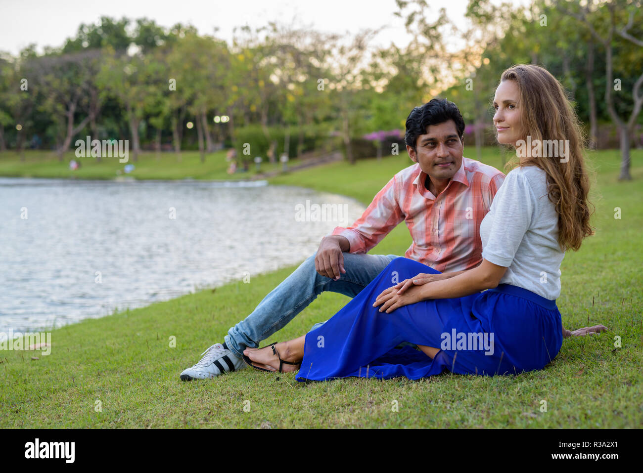 Multi-ethnische Paar denken beim Sitzen in der Wiese gegen Stockfoto