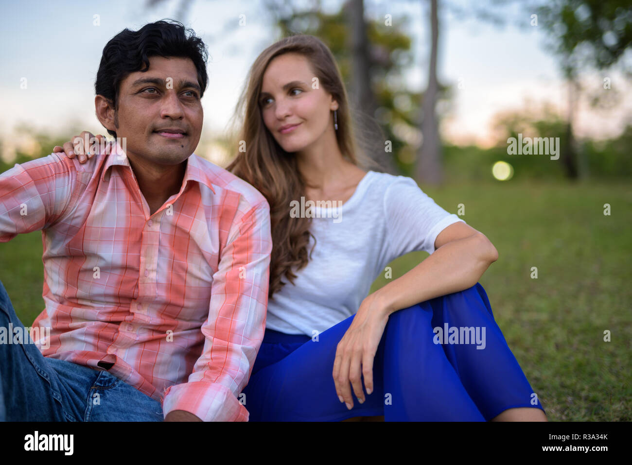 Multi-ethnische Paar sitzen auf der Wiese mit Frau suchen an Stockfoto