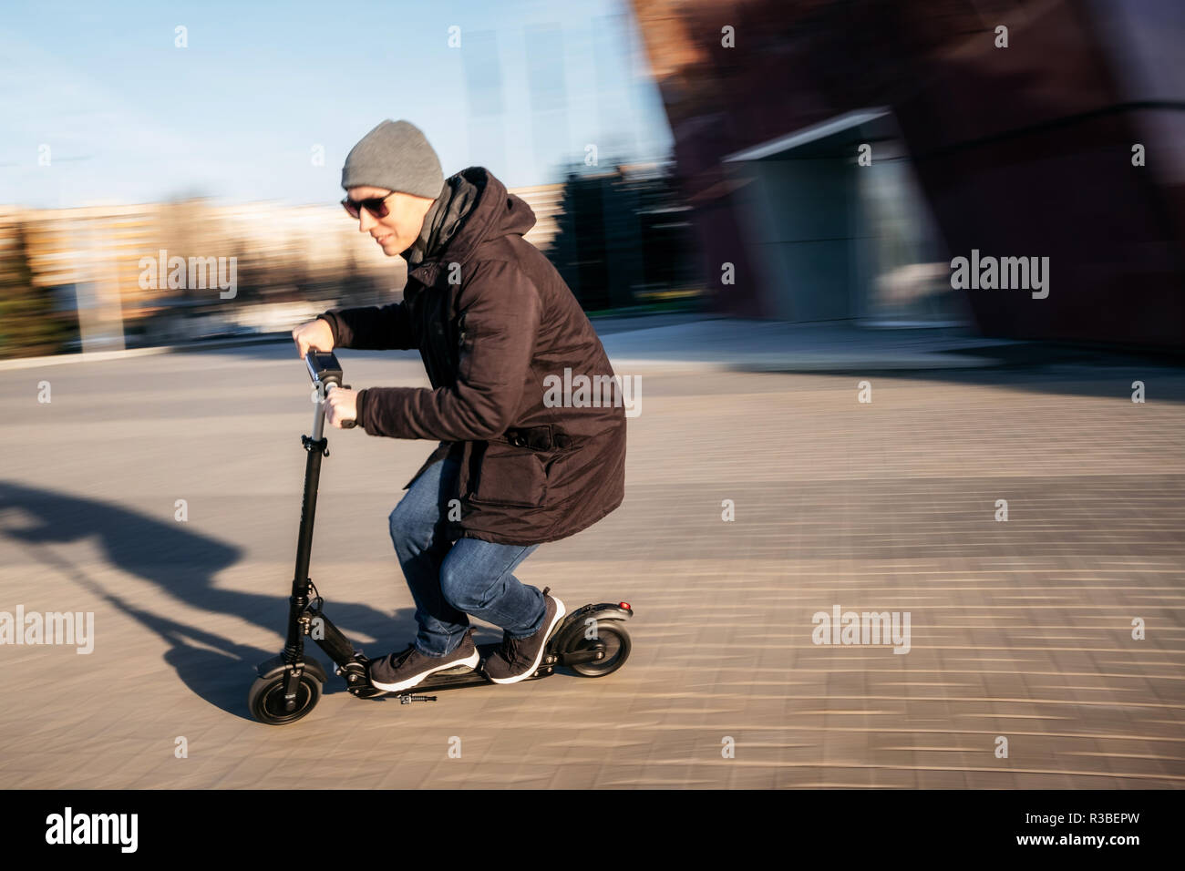 Junger Mann in Freizeitkleidung auf elektrische kick Scooter auf Stadt Straße in motion blur im Herbst Stockfoto