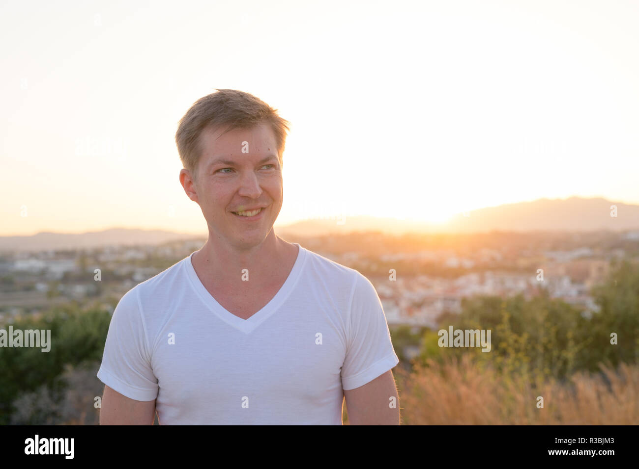 Junge Attraktive touristische Mann lächelnd beim Denken auf der Spitze des Hügels Stockfoto